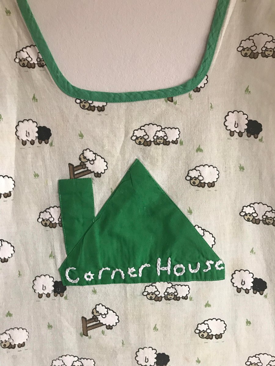 A green Corner House apron with a sheep print